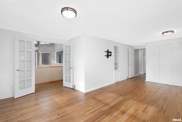 unfurnished room featuring french doors, light hardwood / wood-style floors, built in shelves, and a textured ceiling