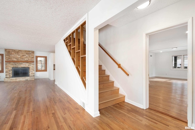 stairs featuring a fireplace, wood-type flooring, and a textured ceiling