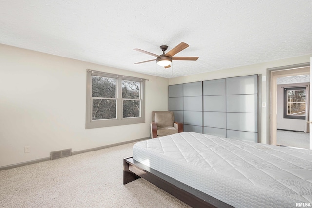 bedroom with ceiling fan, light carpet, and a textured ceiling