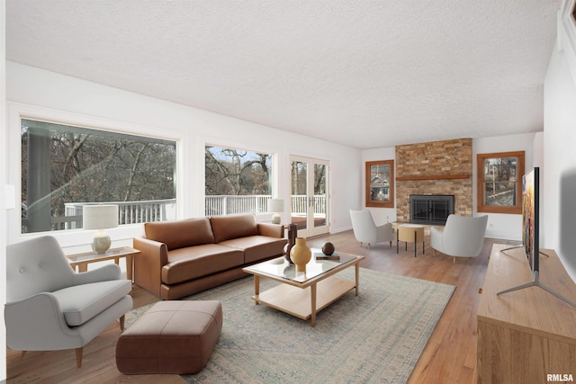 living room with a stone fireplace, wood-type flooring, and a textured ceiling