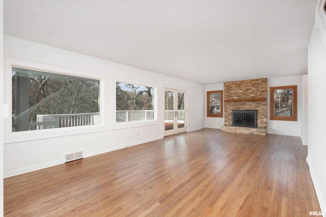 unfurnished living room featuring hardwood / wood-style flooring, a stone fireplace, and a textured ceiling