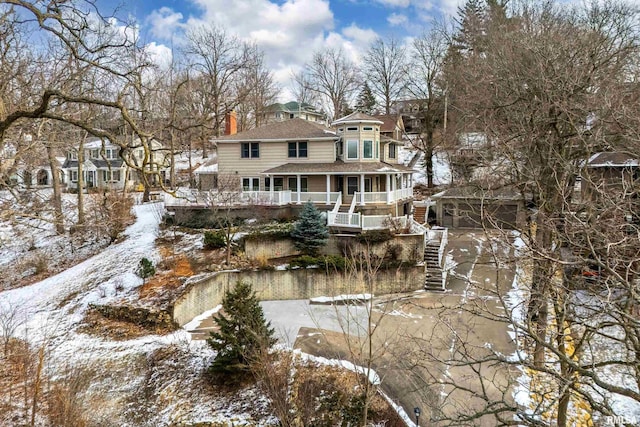 snow covered back of property featuring a garage and covered porch