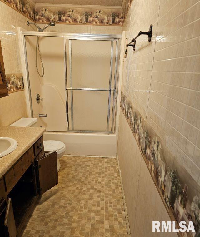 full bathroom featuring vanity, combined bath / shower with glass door, tile walls, and toilet