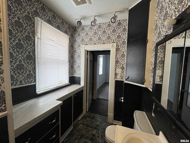 bathroom with track lighting, toilet, and a textured ceiling