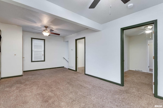 carpeted spare room featuring beamed ceiling and ceiling fan