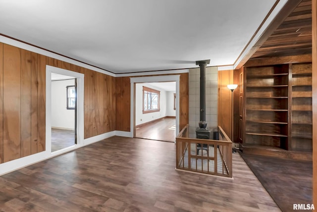 unfurnished living room featuring built in features, a wood stove, ornamental molding, dark hardwood / wood-style flooring, and wood walls