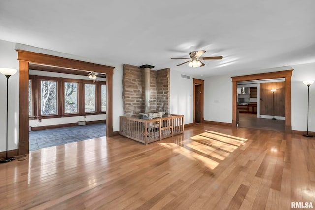 unfurnished living room with wood-type flooring, a wood stove, and ceiling fan