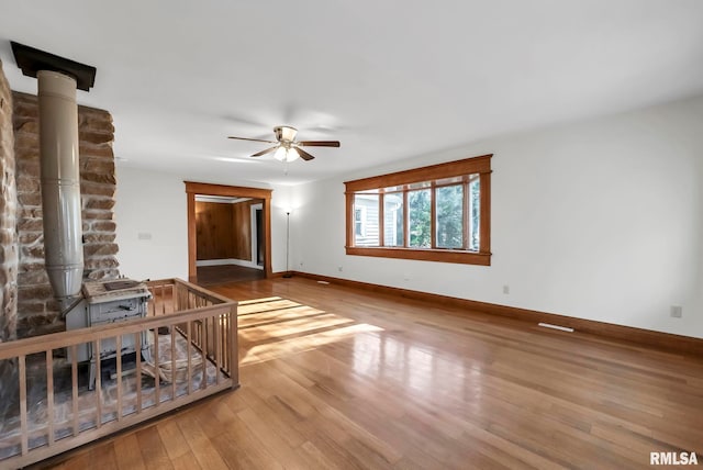 unfurnished living room featuring a wood stove, ceiling fan, and light hardwood / wood-style flooring