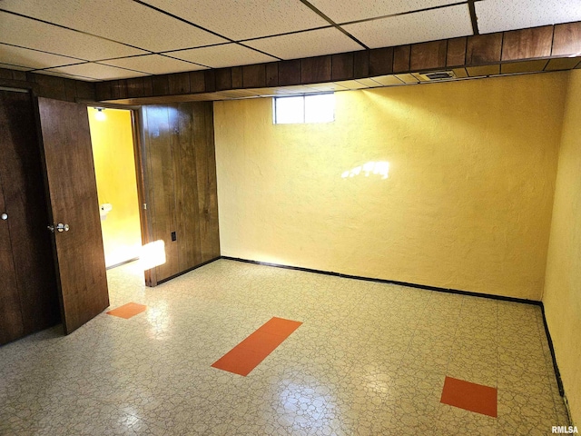 basement featuring a paneled ceiling and wood walls