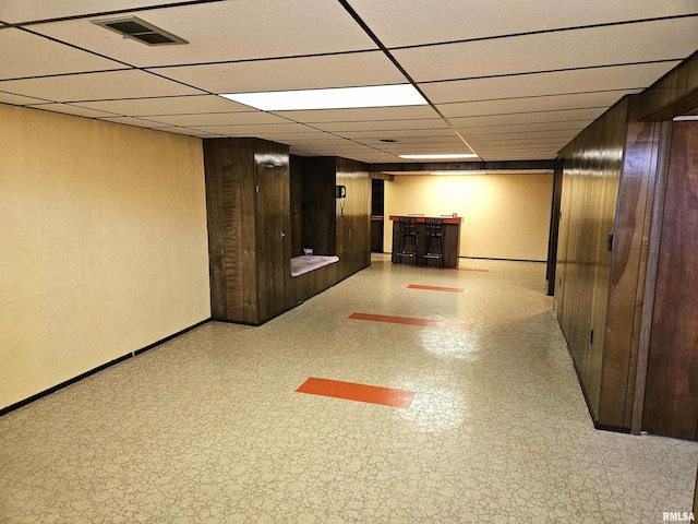 basement featuring bar area, a drop ceiling, and wooden walls