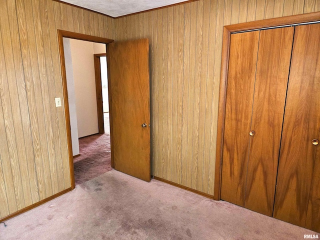 unfurnished bedroom featuring light carpet, a closet, and wood walls