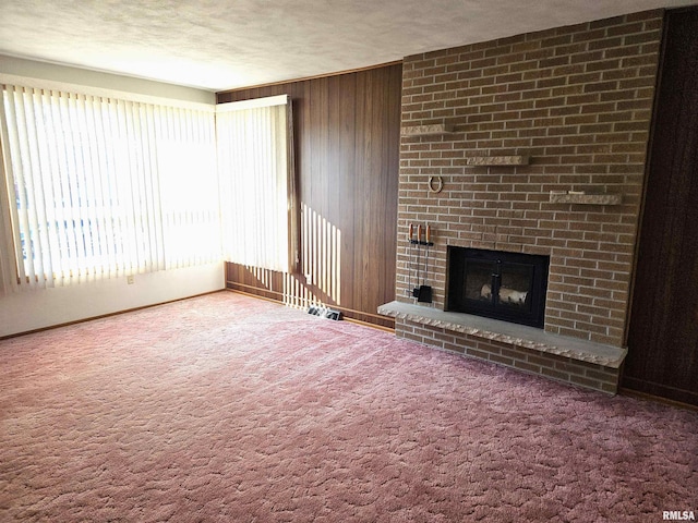 unfurnished living room featuring carpet floors, a fireplace, a textured ceiling, and wood walls