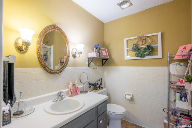 bathroom with tile walls, vanity, toilet, visible vents, and wainscoting