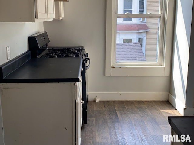 kitchen with black gas range oven, wood-type flooring, and white cabinets