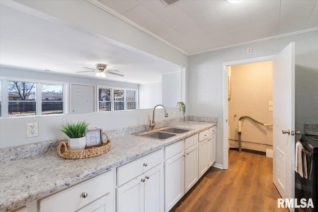 kitchen with black range with electric cooktop, wood finished floors, a sink, white cabinets, and ornamental molding