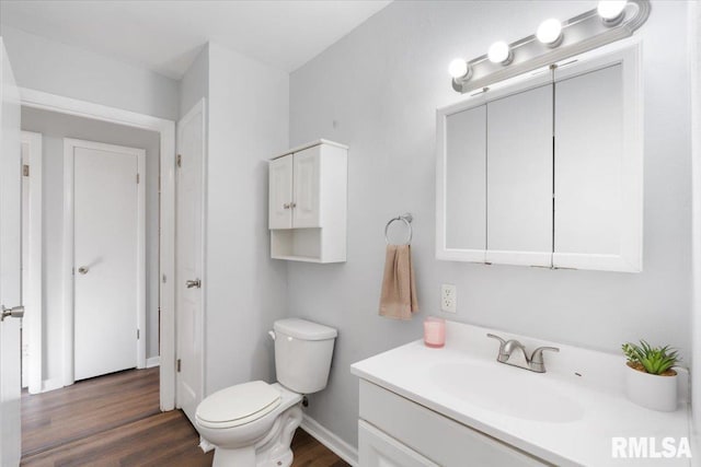 bathroom featuring toilet, baseboards, wood finished floors, and vanity