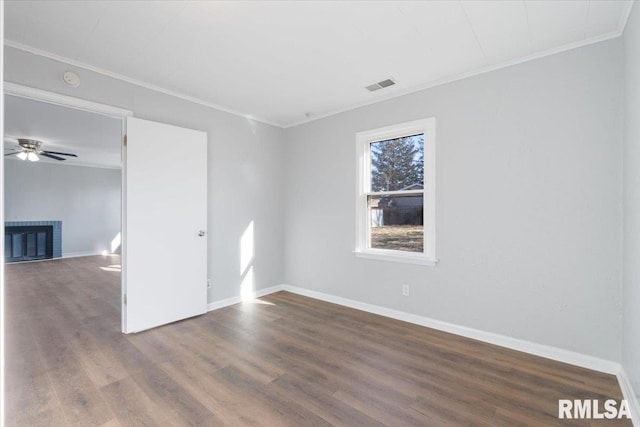 empty room with a brick fireplace, visible vents, wood finished floors, and ornamental molding