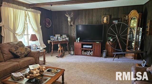 carpeted living room with beamed ceiling and wooden walls