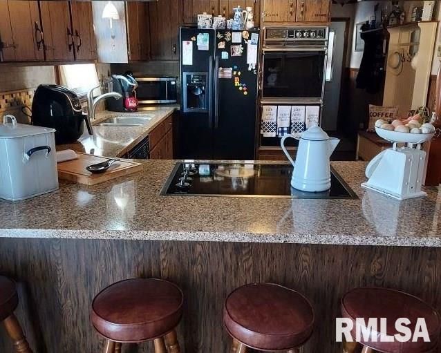 kitchen featuring sink, a kitchen bar, and black appliances