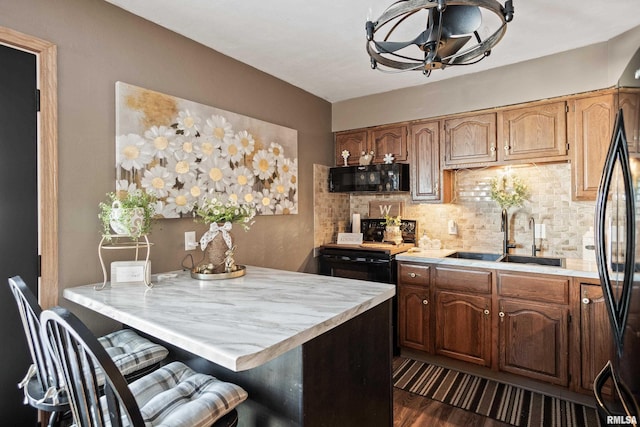 kitchen featuring sink, a kitchen breakfast bar, dark hardwood / wood-style floors, black appliances, and decorative backsplash