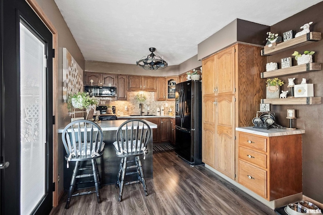 kitchen featuring sink, a kitchen breakfast bar, dark hardwood / wood-style floors, tasteful backsplash, and black appliances