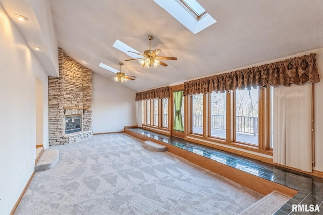 unfurnished living room featuring dark colored carpet, ceiling fan, a fireplace, and a skylight