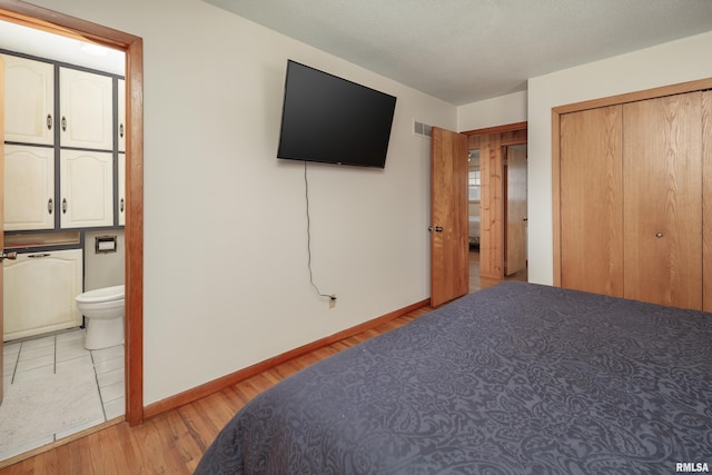 bedroom with ensuite bathroom, light hardwood / wood-style floors, and a closet