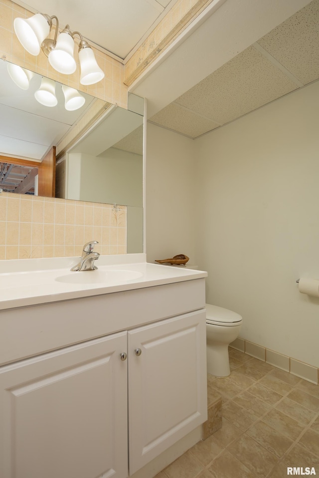 bathroom with backsplash, vanity, toilet, a drop ceiling, and tile patterned floors