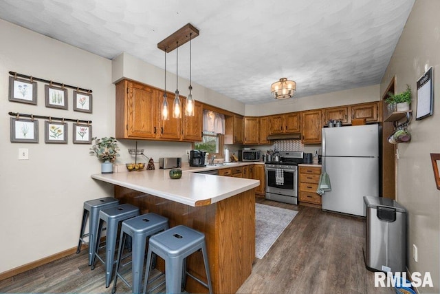 kitchen featuring appliances with stainless steel finishes, pendant lighting, dark hardwood / wood-style flooring, a kitchen breakfast bar, and kitchen peninsula