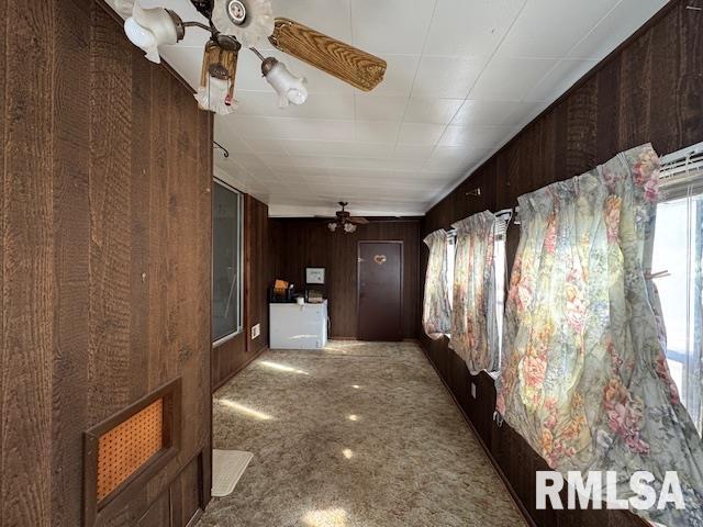 hall featuring light colored carpet, wooden walls, and a wealth of natural light