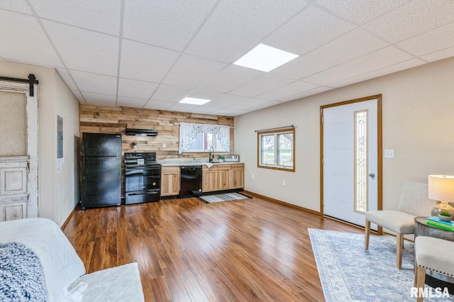 kitchen featuring wood walls, sink, dark hardwood / wood-style flooring, black appliances, and a drop ceiling