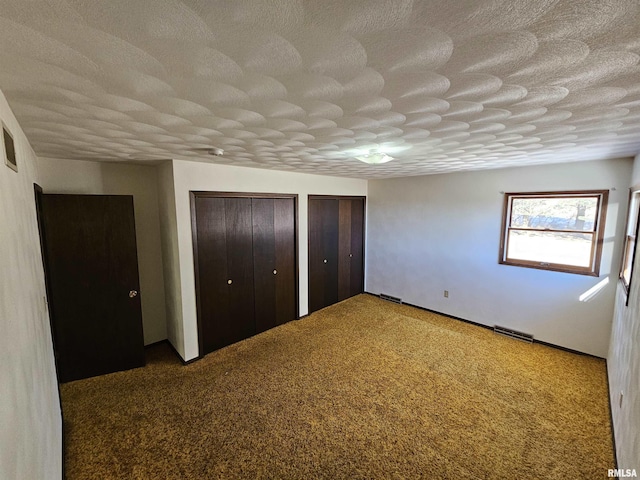 unfurnished bedroom with multiple closets, dark carpet, and a textured ceiling