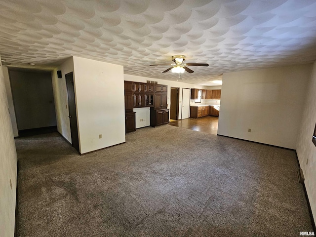 unfurnished living room featuring ceiling fan, a textured ceiling, and dark colored carpet