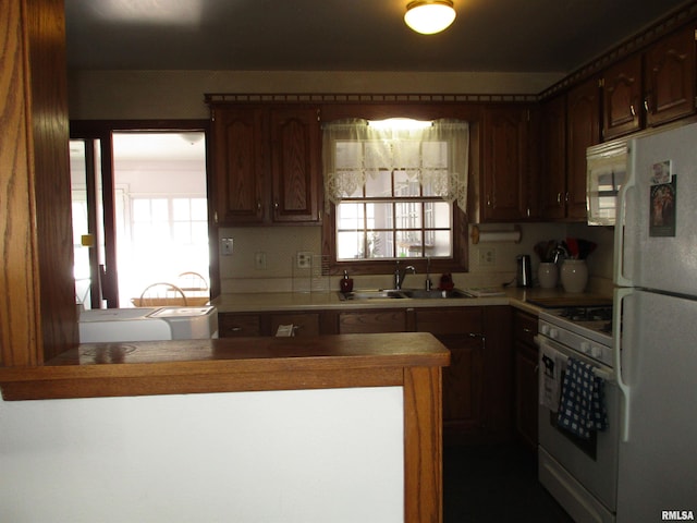 kitchen with a healthy amount of sunlight, sink, white appliances, and kitchen peninsula