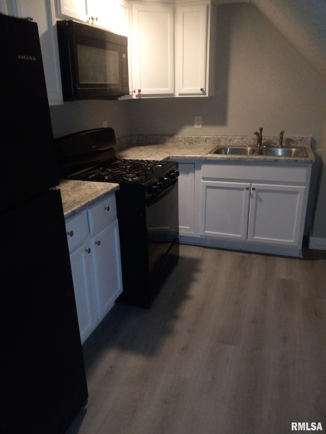 kitchen featuring vaulted ceiling, white cabinetry, wood-type flooring, sink, and black appliances