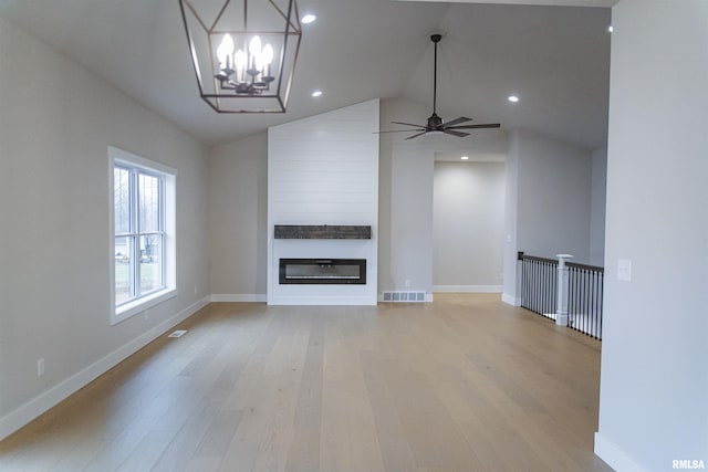 unfurnished living room featuring a large fireplace, lofted ceiling, ceiling fan with notable chandelier, and light wood-type flooring