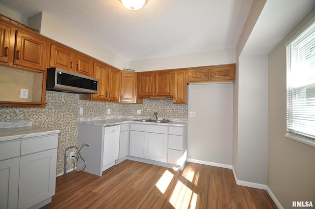 kitchen featuring sink, a textured ceiling, white dishwasher, light hardwood / wood-style floors, and backsplash