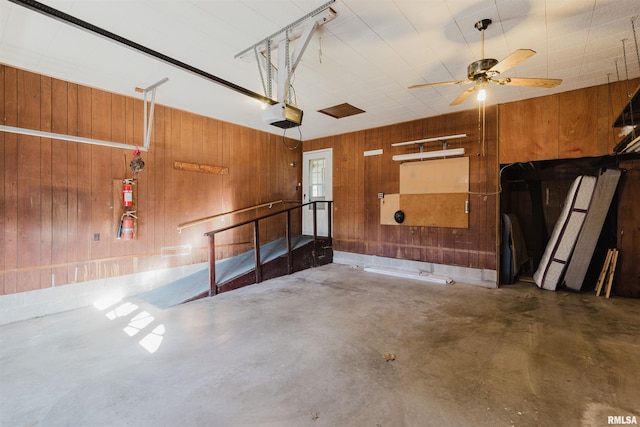 garage featuring a garage door opener, ceiling fan, and wooden walls