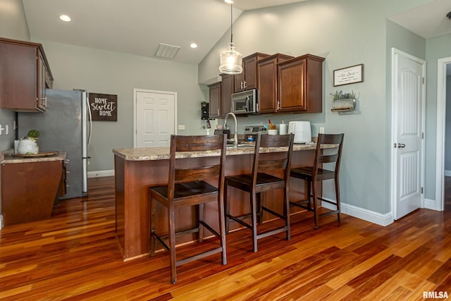 kitchen with appliances with stainless steel finishes, decorative light fixtures, kitchen peninsula, light stone countertops, and dark wood-type flooring