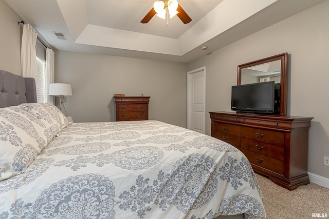 bedroom with light colored carpet, a raised ceiling, and ceiling fan