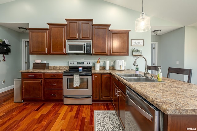 kitchen featuring dark wood-type flooring, sink, hanging light fixtures, appliances with stainless steel finishes, and a kitchen island with sink