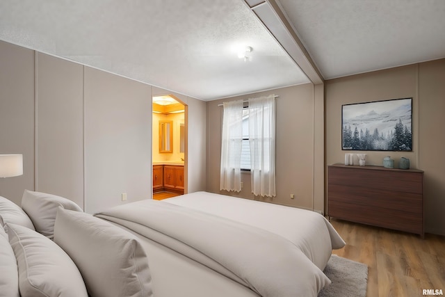 bedroom featuring ensuite bath, a textured ceiling, and light wood-type flooring