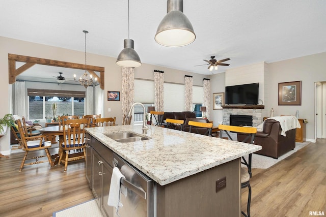 kitchen featuring a stone fireplace, decorative light fixtures, sink, stainless steel dishwasher, and a center island with sink