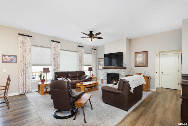 living room featuring ceiling fan, dark hardwood / wood-style flooring, and a stone fireplace