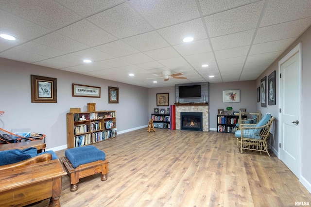 sitting room featuring ceiling fan, wood-type flooring, a fireplace, and a drop ceiling