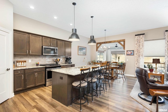 kitchen with decorative light fixtures, a center island with sink, dark brown cabinets, and appliances with stainless steel finishes