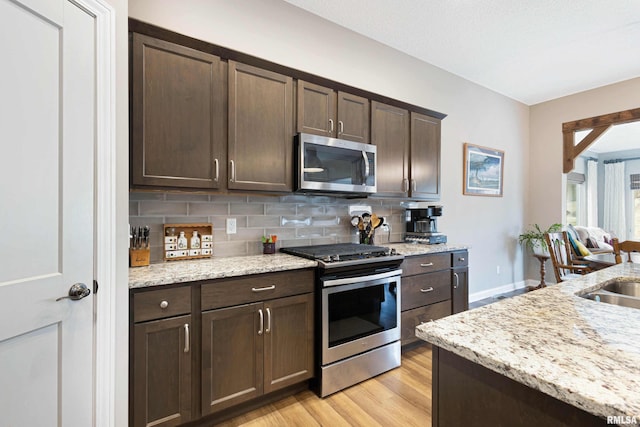 kitchen featuring appliances with stainless steel finishes, dark brown cabinets, light stone counters, and decorative backsplash