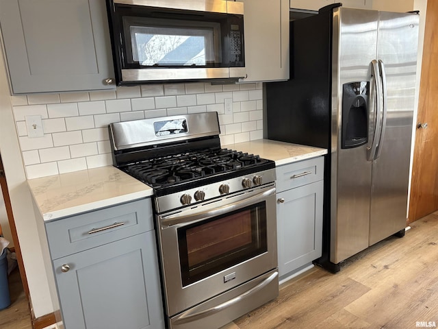 kitchen with decorative backsplash, gray cabinets, stainless steel appliances, and light hardwood / wood-style floors