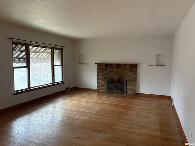 unfurnished living room featuring hardwood / wood-style flooring and a brick fireplace