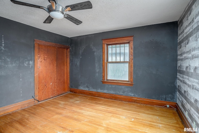 empty room with ceiling fan, a textured ceiling, and light wood-type flooring